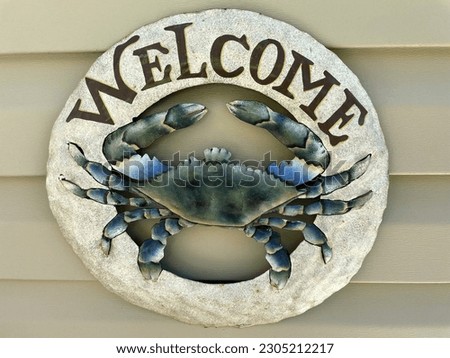 Outdoor welcome sign with the images of a blue crab at the center that screams beach motif. 