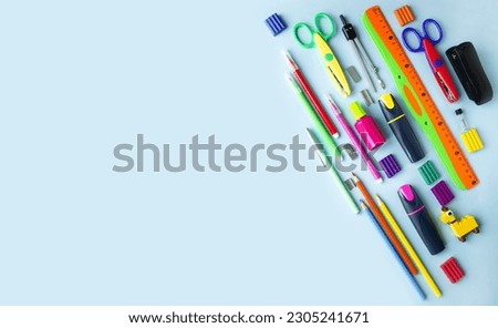On a blue background, a flat layout of stationery for school, colored pencils, felt-tip pens, a ruler, an eraser, scissors.  Back to school concept.  Space for copy text.