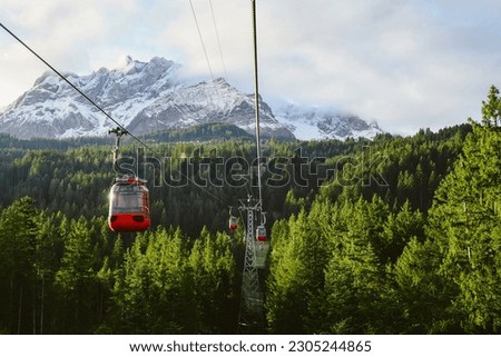 red cable car Surrounded by lush green pines, thick clouds, behind snow-capped mountains, Kriens, Switzerland. Royalty-Free Stock Photo #2305244865