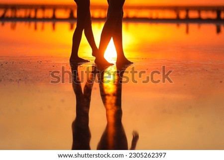 Summer travel holiday. Cropped photo of silhouette legs mom and child daughter walk together on sunset beach. Reflection on water. Mothers day. Concept of family values. International Children's Day.