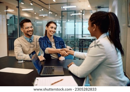 Young happy couple closing a deal with their insurance agent on a meeting in the office. Women are handshaking. Royalty-Free Stock Photo #2305282833