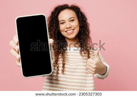 Young woman of African American ethnicity wear light casual clothes hold in hand use close up mobile cell phone with blank screen workspace area show thumb up isolated on plain pastel pink background