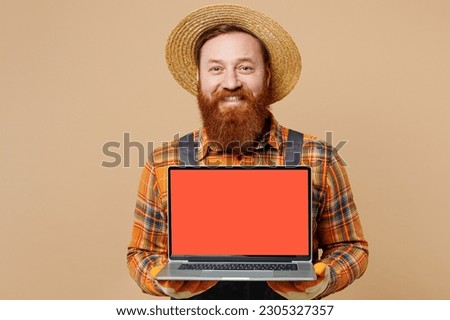 Young happy man wearing straw hat overalls work in garden hold use blank screen workspace laptop pc computer show thumb up isolated on plain pastel light beige color background. Plant caring concept