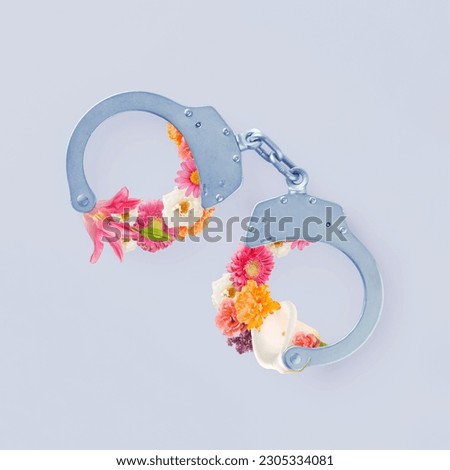 Metallic handcuffs closed with wreath of blooming colorful flowers on isolated pastel gray background. Minimal flat lay. Abstract concept of soft power, liberty illusion, diplomatic influence or love.