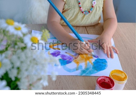 children's hand paints with brush, small child, little girl preschooler 3 years creates bright picture on paper, childish naive drawing in colored watercolor, gouache, acrylic, happiness childhood