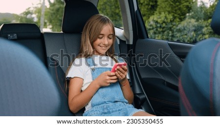 Pretty teenage girl 10-year-old girl sitting backseat in car and using phone Beautiful little girl using a smartphone browsing internet and writes a message to friends. Royalty-Free Stock Photo #2305350455