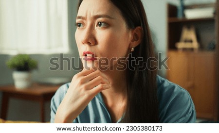 Thoughtful young Asian woman deep thinking on sofa in cozy living room. Female adult looking around bored and tired considering serious plan trying to solve problem in mind, portrait close up concept Royalty-Free Stock Photo #2305380173