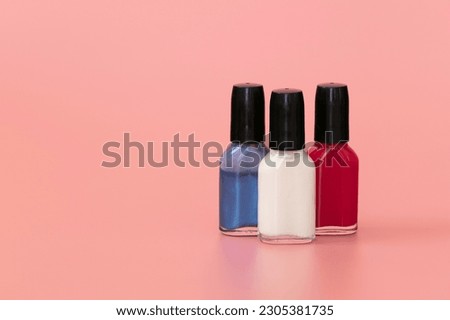 Red, white and blue nail polish bottles on pink background. Copy space.