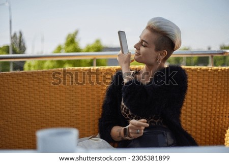Cheerful diverse woman with short hair taking a picture with a smart phone outdoor. Portrait of a beautiful tom boy female in a street restaurant