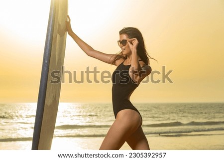Portrait of happy young woman relaxing on tropical beach. Smiling girl with fashion sunglasses enjoying vacation on Bali, Indonesia. Surfing picture for social media promo.