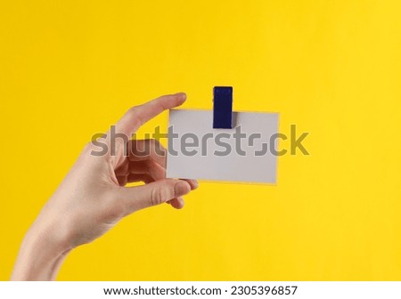 Hand holds a badge on a clip, yellow background