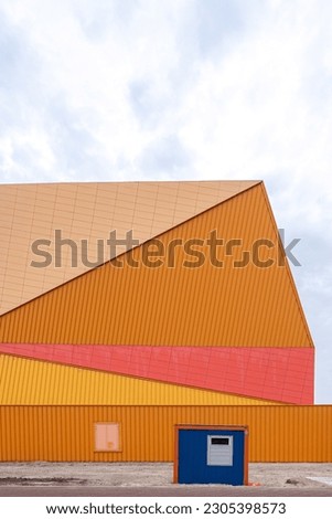 Abstract photo of a public building with orange tones and clean lines, there is a small blue building in front of it