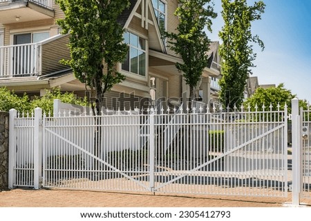 Iron front gate of a complex townhouses. Wrought iron white gate in neighborhood. Street photo. Metal garden entrance gates with fence. Classical design white wrought iron gate in suburb of Vancouver