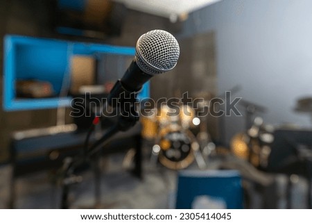 Microphone in a recording studio with a blurred background including a drum kit.
