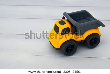 Toy childrens dump truck  on a white wooden background.Yellow and grey miniature car.Selective focus.