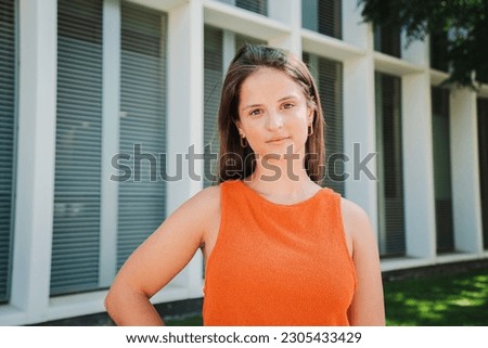 Serious young Caucasian teenage female looking at camera having relaxed emotion and gentle facial expression outside. Portrait of confident serene woman posing for photo standing with hand on hip