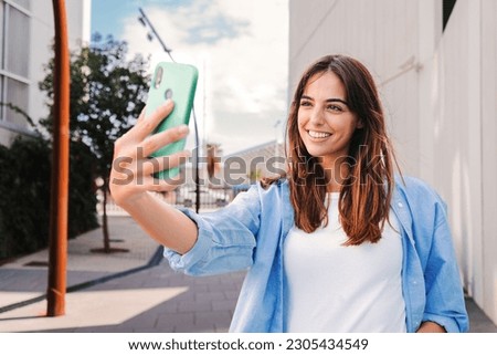 Happy young teenage female looking at camera and taking a selfie on smartphone showing a toothy smile. Portrait of laughing woman shooting a photo or record video with cellphone for social media. High