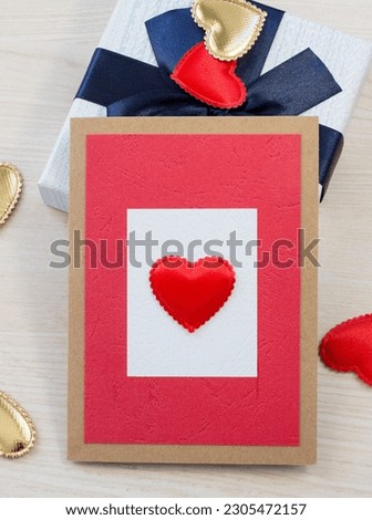 Red postcard with a heart on a white insert in a brown frame on a light brown wood texture background