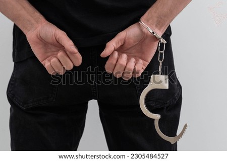 arrested man with cuffed hands behind prison bars. Royalty-Free Stock Photo #2305484527
