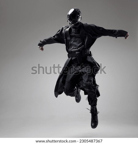 Urbantech outfit cyber style, a young man in stylish black clothes and a mirror mask on his whole face, in a jump. Studio photo on a light background