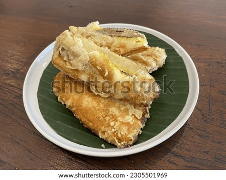 close up deep fried bananas on banana leaf and plate with wooden table backgroud. Top angle, pisang goreng