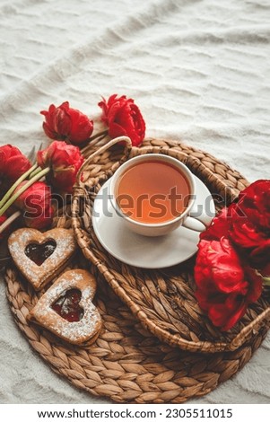 Tray with tasty breakfast, bouquet of peonies and gift for Valentine's Day on bed.