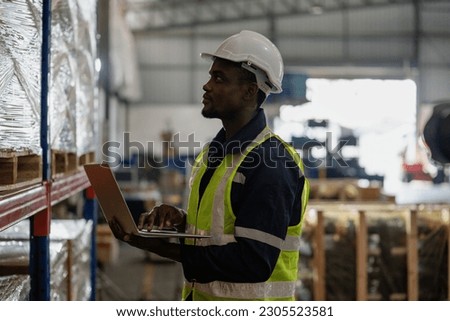 Handsome warehouse worker uses digital laptop for checking stock, on the shelves standing cardboard boxes