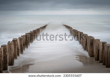 Wave breakers on the beach of Domburg in the Netherlands. Long exposure photo with dynamic waves breaking at the shore on wooden poles