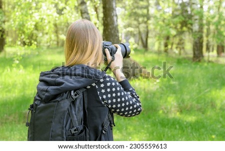 Girl with a digital camera in the forest taking photos, shot from behind