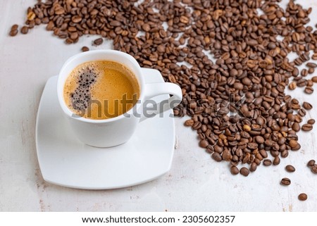 A white cup of black coffee on a background of roasted beans. A picture for a coffee shop. Top view of a cup of coffee.