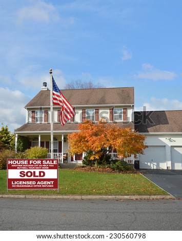 American Flag Pole Real Estate Sold (another success let us help you buy sell your next home) sign on front yard lawn of suburban colonial style home autumn day residential neighborhood blue sky USA