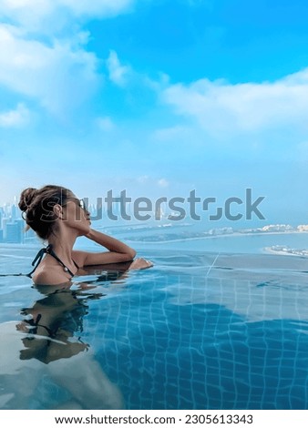 Beautiful brunette girl in a swimsuit with a slender figure, plump lips, in sunglasses. A girl in an infinite pool against the backdrop of a beautiful city. Sky clouds sea, vacation beach summer Dubai