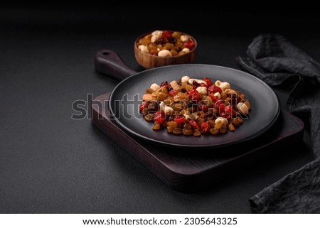 Mix of roasted cashews, hazelnuts and walnuts with dried cranberries and raisins on a dark concrete background