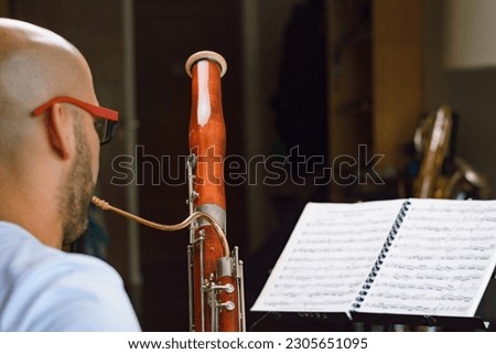 rear view of bassoonist man, studying and practicing music, he is reading sheet music and playing bassoon at home, focus on bassoon, music concept, copy space. Royalty-Free Stock Photo #2305651095
