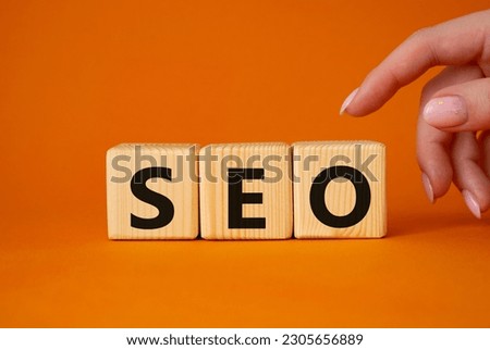 SEO - Search Engine Optimization symbol. Wooden blocks with words SEO. Businessman hand. Beautiful orange background. Business and SEO concept. Copy space.