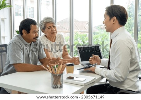 Asian young employee use digital tablet and laptop computer while offering about life insurance plan to Mature couple