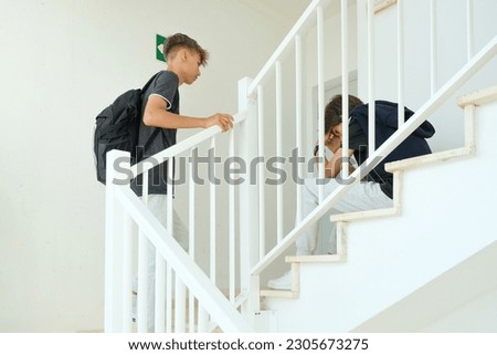 Teenager comforting consoling upset sad boy in staircase. Education, bullying, conflict, social relations, problems at school, learning difficulties concept Royalty-Free Stock Photo #2305673275