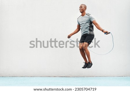 Jump, rope and space with black man skipping in stadium for sports, workout and cardio. Performance, health and body with male athlete training on track for strong, mockup and exercise by wall Royalty-Free Stock Photo #2305704719