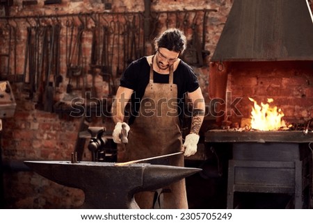 Worker, blacksmith and metal forge in workshop and manual working on hot steel with hammer, fire and sparks. Man, welding job or iron tools manufacturing and expert, trade and dark workspace Royalty-Free Stock Photo #2305705249