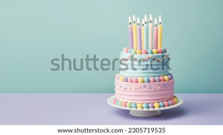 Pastel colored tiered birthday cake decorated with candies and colorful candles with pastel buttercream frosting against a plain turquoise background