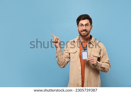 Smiling man showing VIP pass badge on light blue background, space for text