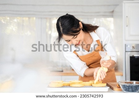 Small business entrepreneur asian woman bakery shop making fruit tart. Female Baker Using Piping Bag to Decorate fruit tart with cream cheese on white kitchen counter.indoor lifestyle concept. Royalty-Free Stock Photo #2305742593