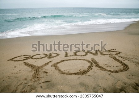 GOD LOVES YOU. Words written in beach sand. The words GOD LOVES YOU written in the sand on the beach with the ocean as the background. God's Love is all you need. Everyone Loves the beach. 