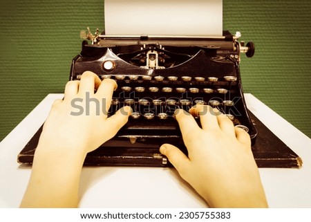 Hands of anonymous young person are typing on vintage typewriter filled with white blank sheet of paper on white table against a green wall. Concept of journalist work history, creativity, inspiration