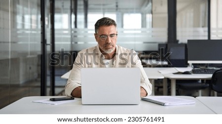 Mature Indian or Latin business man trader using computer, typing, working in modern office, doing online internet research on laptop. Horizontal photo with copy space banner for website header design Royalty-Free Stock Photo #2305761491