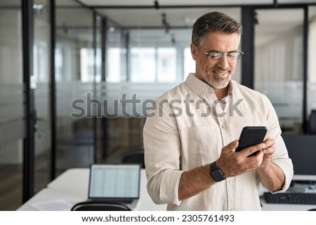 Copy space are with smiling mature Latin or Indian businessman holding smartphone in office. Middle aged manager using cell phone mobile app. Digital technology application and solutions for business.