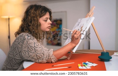 Young woman artist is painting in relax with tempera watercolor paints a bird portrait picture in her studio.
Wide and detailed close-up shots of the brushes, palette, paint tubes and canvas.