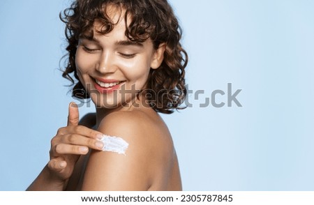 Body skin care. Smiling woman applying body cream portrait. Beautiful happy girl model with cosmetic moisturizing lotion on perfect hydrated soft skin on shoulder at studio, blue background. Royalty-Free Stock Photo #2305787845