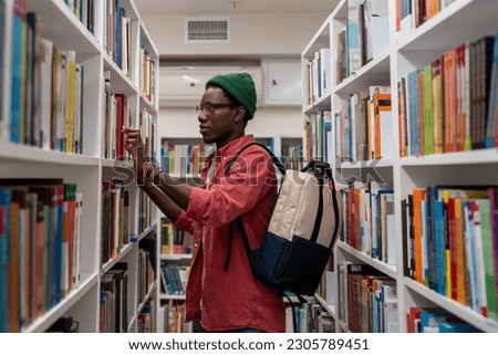 Interested Black student man choosing book for reading in bookstore. Focused young African American guy searching materials for educational research in college library. Literature and education