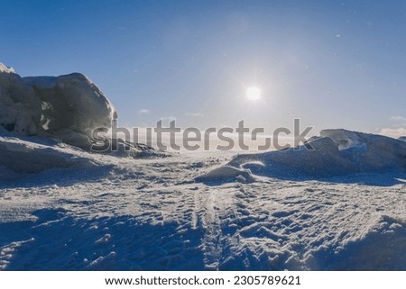Winter landscape. Panoramic view of beautiful sunset on bay. Ice, snow and rocks on coastline. Setting sun in bright light. High quality photo